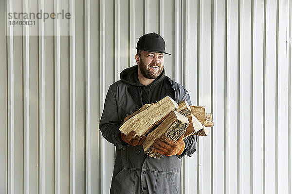 Glücklicher Koch mit Brennholz vor der Wand