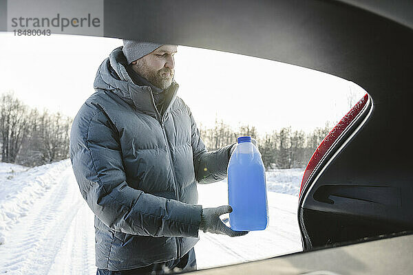 Mann holt im Winter eine Flasche Frostschutzmittel aus dem Kofferraum