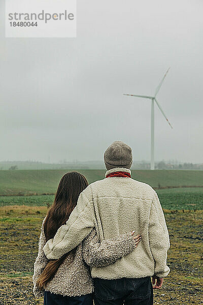 Teenager-Paar steht zusammen und schaut auf die Windkraftanlage
