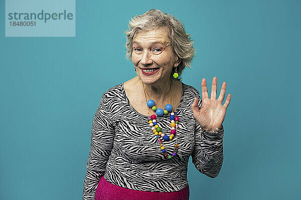Happy senior woman waving against turquoise background
