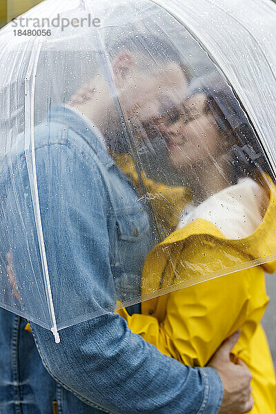 Zärtliches umarmendes Paar  gesehen durch einen nassen transparenten Regenschirm