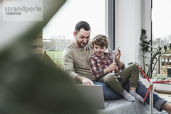 Vater schaut auf Laptop  während Sohn zu Hause sitzt