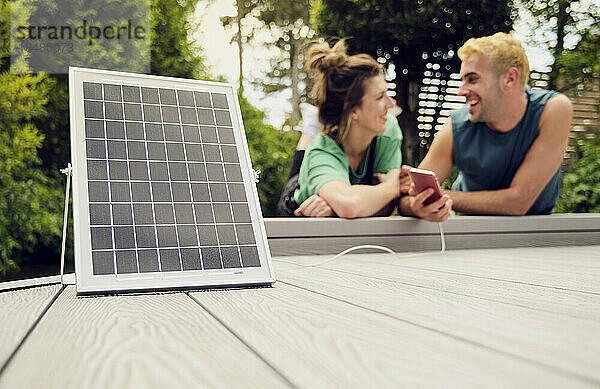 Frau mit Freund lädt Smartphone mit Solarpanel auf