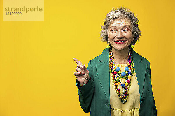Lächelnde ältere Frau gestikuliert vor gelbem Hintergrund