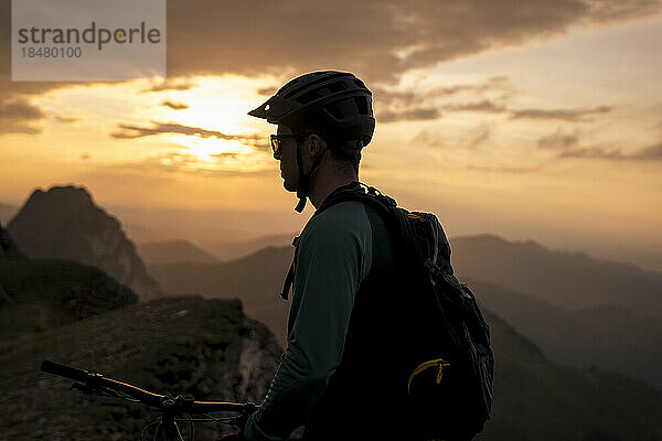 Mountainbiker unter bewölktem Himmel bei Sonnenuntergang