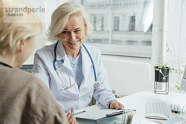 Lächelnder reifer Arzt  der mit dem Patienten über das Dokument spricht