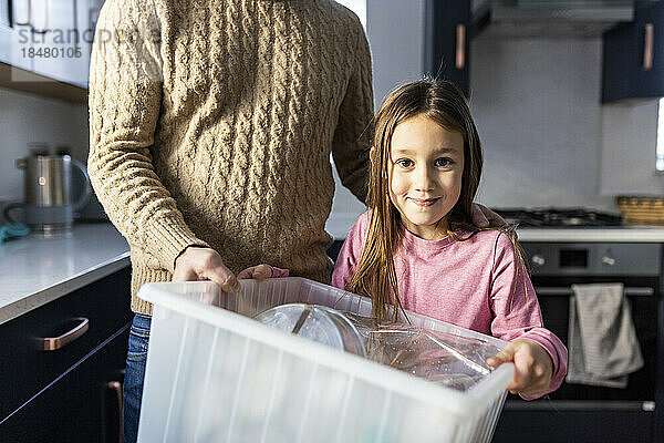 Glückliches Mädchen mit Vater  der zu Hause Plastik recycelt