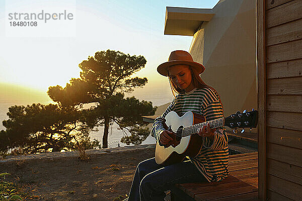 Junge Frau spielt Gitarre bei Sonnenuntergang