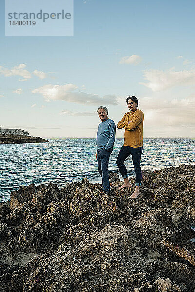 Älterer Mann steht mit Sohn auf einem Felsen vor dem Meer