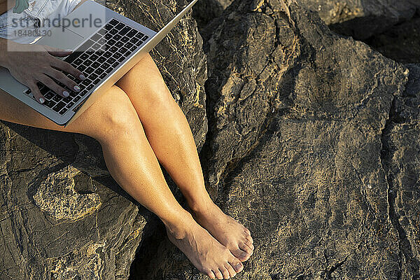 Frau sitzt an einem sonnigen Tag mit Laptop auf einem Felsen