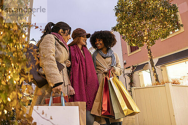 Glückliche Frau mit Einkaufstüten im Gespräch mit Freunden am Fußweg