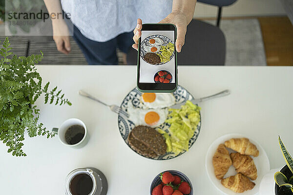 Frau fotografiert zu Hause verschiedene Lebensmittel per Smartphone