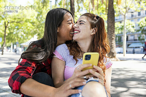 Happy young woman sitting with girlfriend on footpath