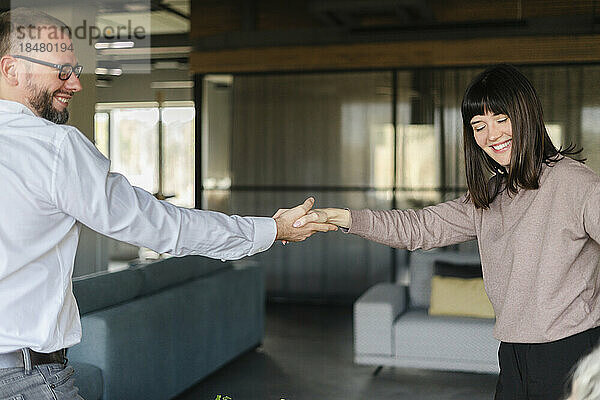 Glücklicher Geschäftsmann und Frau schütteln sich im Büro die Hände