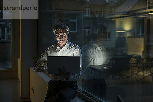 Lächelnder Geschäftsmann  der spät am Laptop im Büro arbeitet