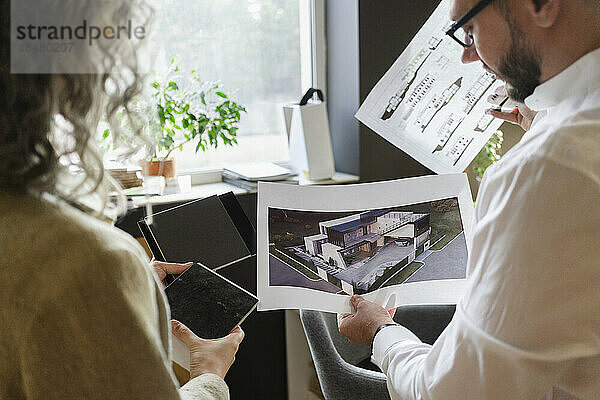 Zwei Kollegen halten den Ausdruck eines Hauses und den Bauplan im Architekturbüro in der Hand