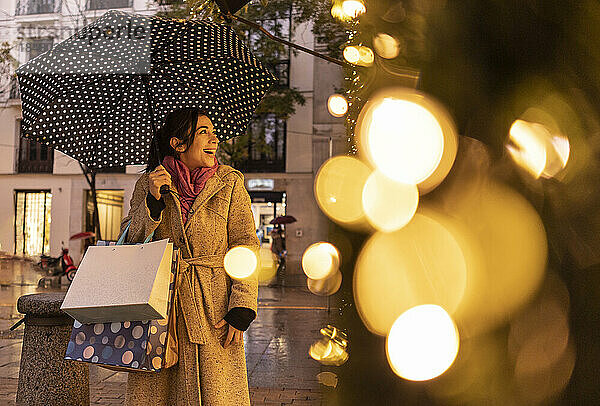Glückliche Frau mit Regenschirm beim Schaufensterbummel am Fußweg