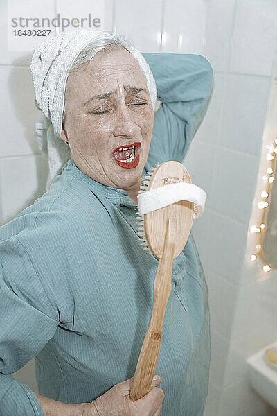 Ältere Frau mit Holzbürste singt im Badezimmer