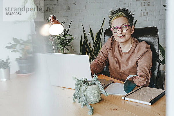 Reife Geschäftsfrau mit Brille sitzt am Schreibtisch im Heimbüro