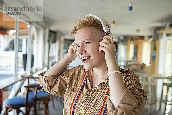 Nicht-binäre Person trägt Kopfhörer und hört im Café Musik