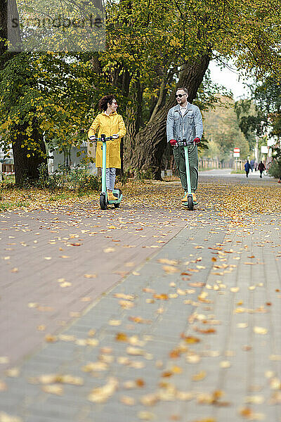 Mann und Frau fahren Elektroroller im Herbstpark