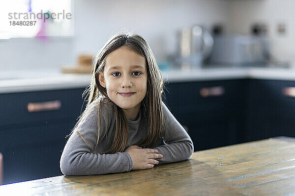 Smiling girl sitting at table in kitchen