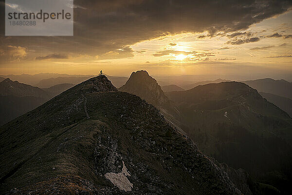 Mountainbiker steht bei Sonnenuntergang auf dem Gipfel