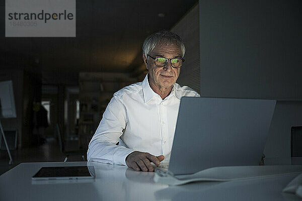 Älterer Geschäftsmann sitzt mit Laptop am Schreibtisch im Büro