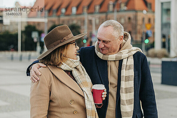 Lächelnder älterer Mann umarmt Frau mit Einwegbecher