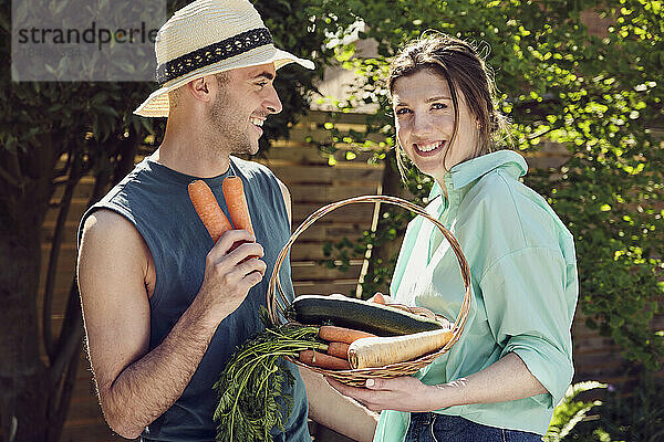 Glückliches junges Paar steht mit einem Korb voller Gemüse im Hinterhof