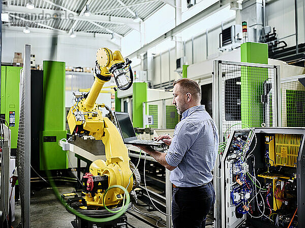 Techniker benutzt Laptop am Roboterarm in einer modernen Fabrik