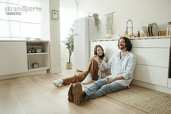Happy couple sitting on floor in kitchen at home