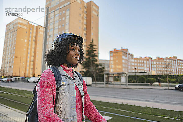 Nachdenkliche junge Frau mit Helm steht vor Gebäuden
