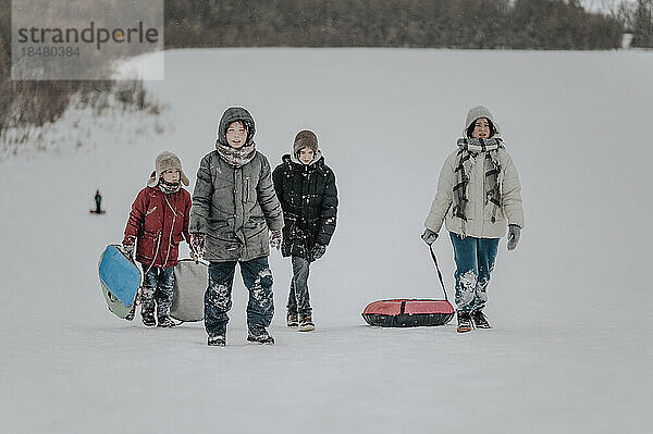 Glückliche Familie  die mit aufblasbarem Schlitten im Schnee spaziert