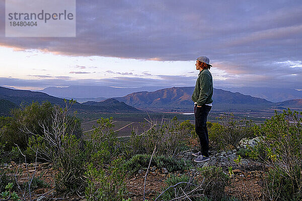 Junger Mann steht bei Sonnenuntergang auf einem Felsen