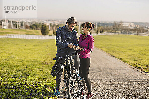 Glückliches Paar mit Fahrrad und Smartphone im Park