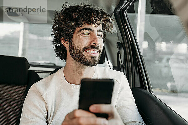 Lächelnder junger Mann mit Smartphone sitzt im Auto