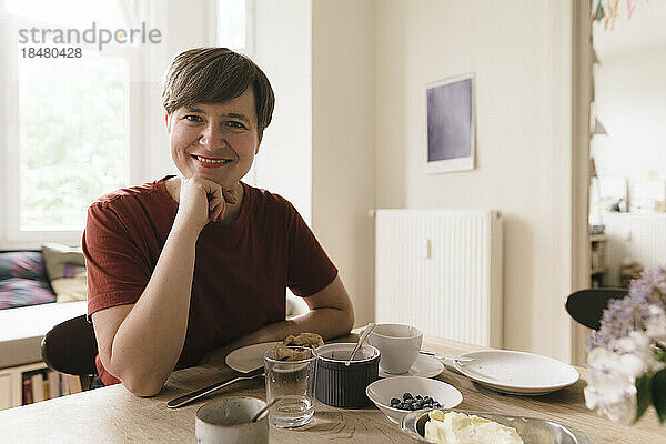 Glückliche Frau mit Frühstück am Esstisch zu Hause