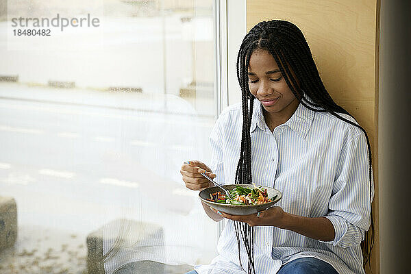 Lächelnde Frau isst Salat am Fenster