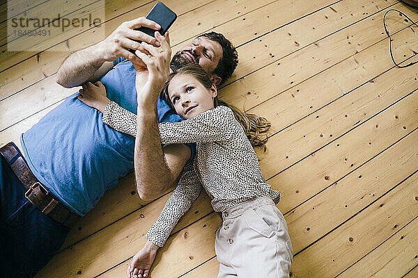 Daughter lying by father using smart phone at home