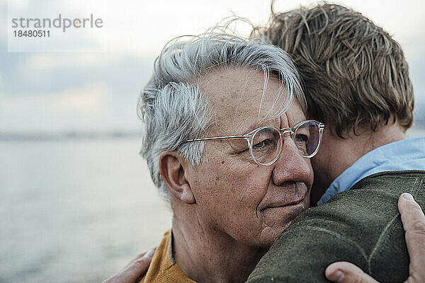 Älterer Mann mit grauem Haar umarmt Sohn