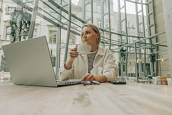 Nachdenkliche Geschäftsfrau hält Tasse am Laptop im Café