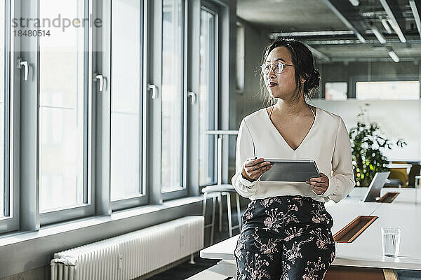 Thoughtful businesswoman holding tablet PC at office