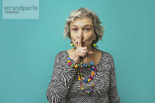 Senior woman with finger on lips standing against colored background