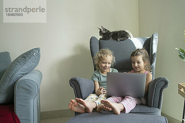 Mädchen schauen sich zu Hause im Sessel einen Laptop an