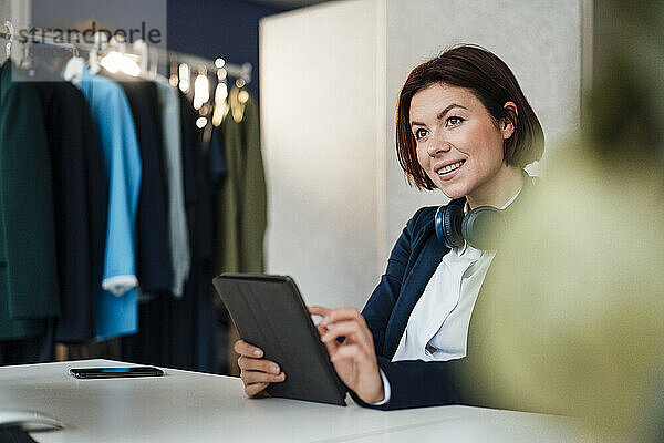 Lächelnde junge Geschäftsfrau sitzt mit Tablet-PC am Schreibtisch im Büro