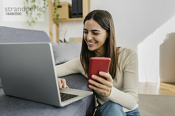 Glückliche junge Frau  die zu Hause Laptop und Smartphone benutzt