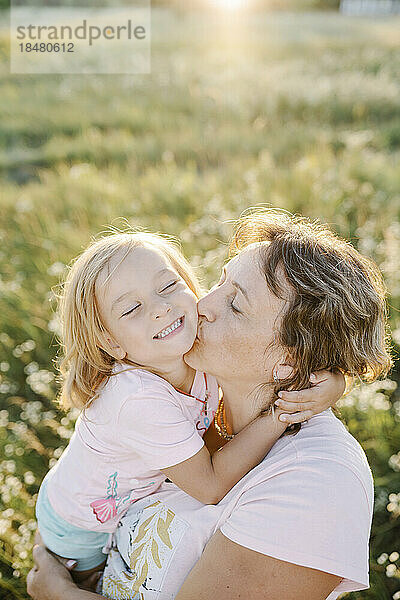 Mother kissing happy daughter in summer field
