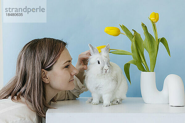 Woman stroking rabbit by tulip vase on table