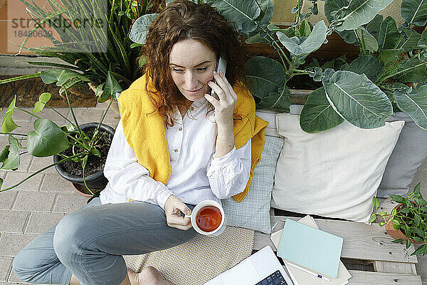 Frau hält eine Tasse Tee in der Hand und telefoniert im Hinterhof